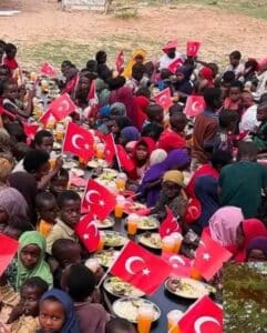 Children at a Merhem food distribution in Somalia eating at long rows of plates lined with small Turkish flags