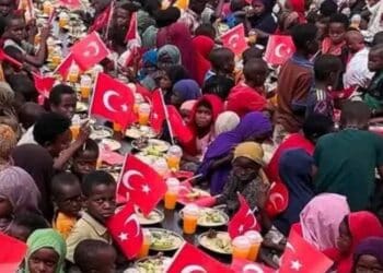Children at a Merhem food distribution in Somalia eating at long rows of plates lined with small Turkish flags