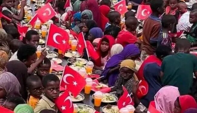 Children at a Merhem food distribution in Somalia eating at long rows of plates lined with small Turkish flags
